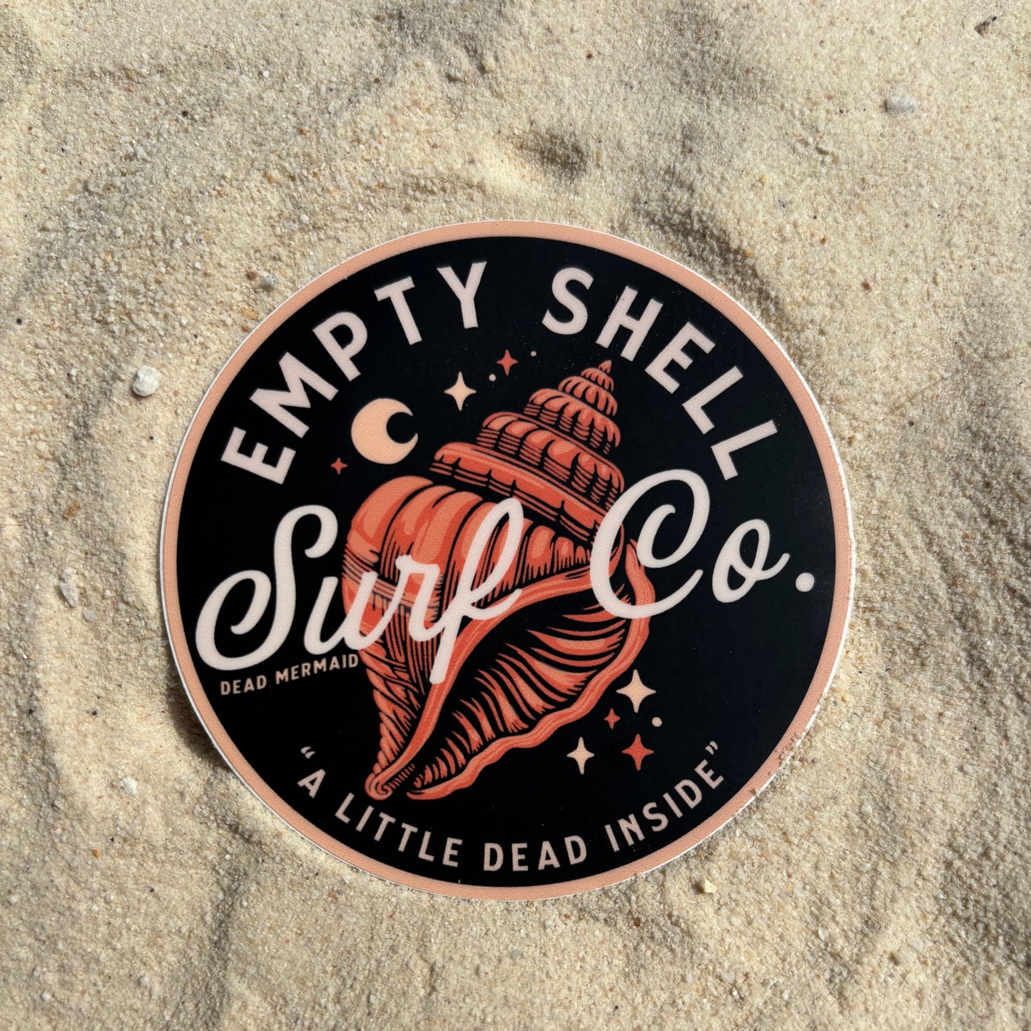Round sticker with shell design and text on sand