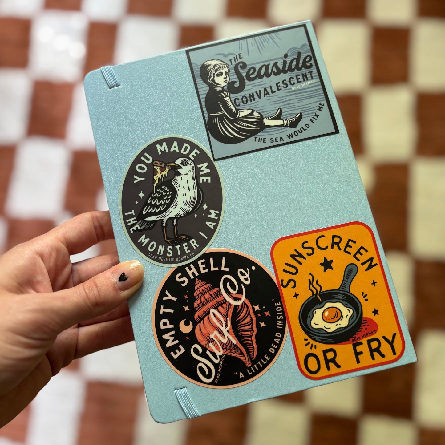 Set of stickers on a light blue card held by a hand against a checkered background