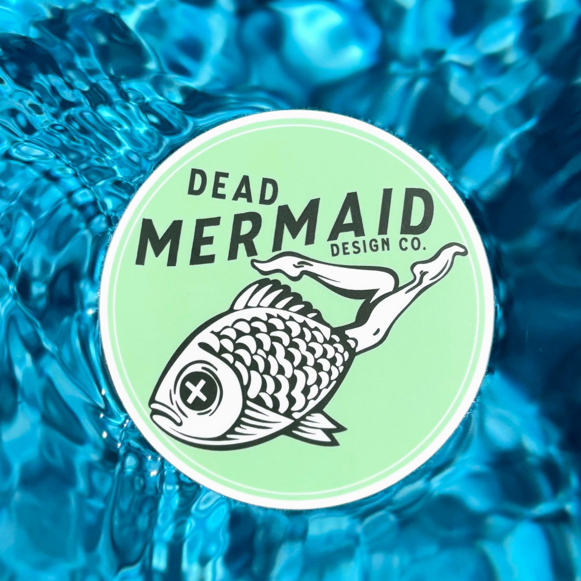 Dead Mermaid Design Co. logo on a light green circle with water background