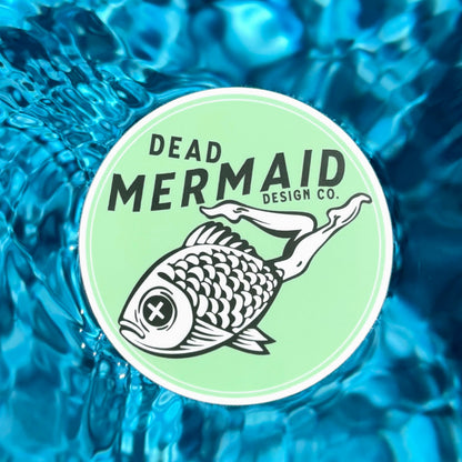 Dead Mermaid Design Co. logo on a light green circle with water background