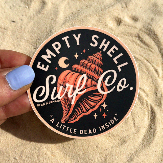 Sticker with 'Empty Shell Surf Co.' design held over sand